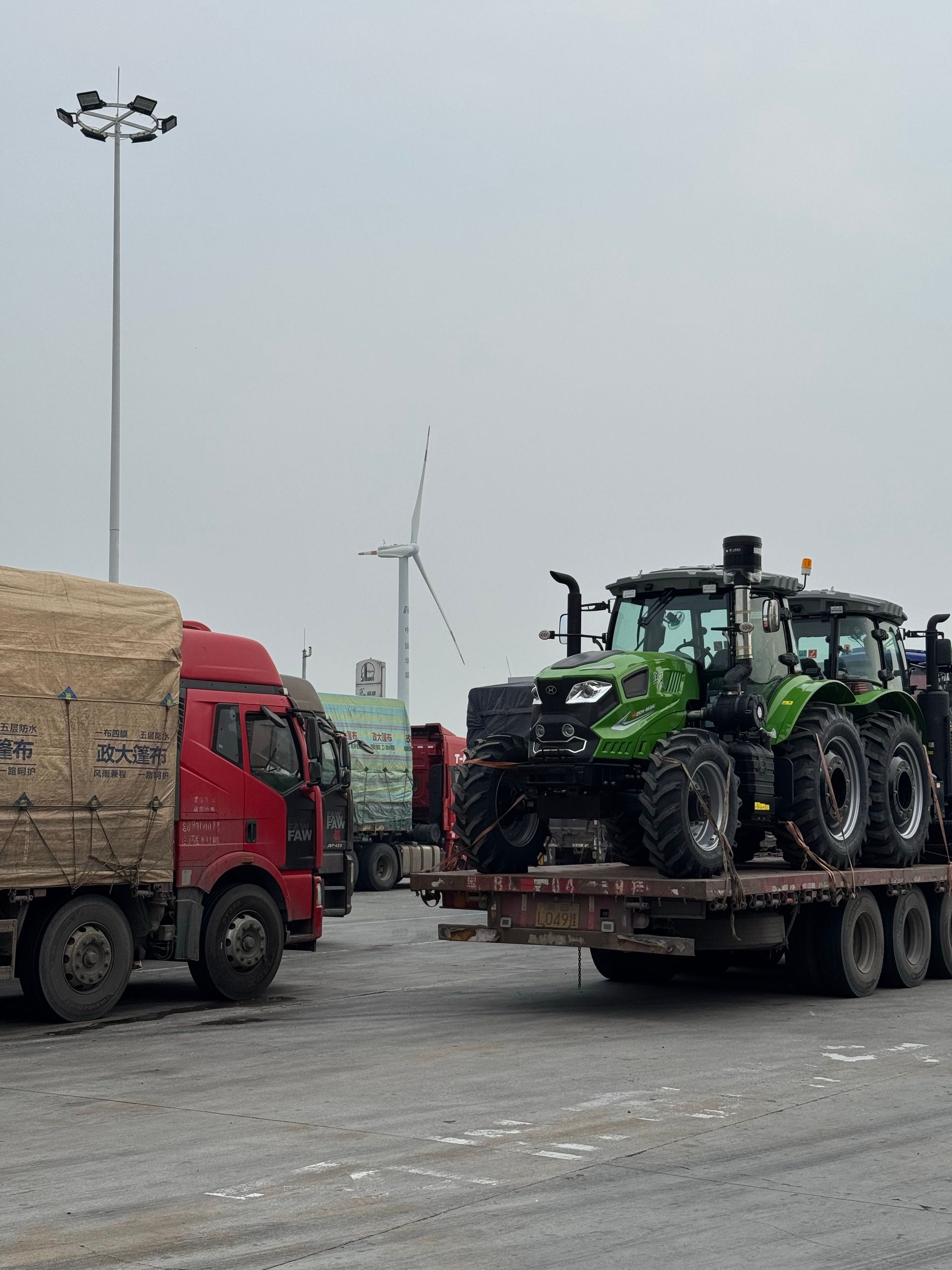 Heavy-duty trucks transporting equipment near wind turbines on a cloudy day.
